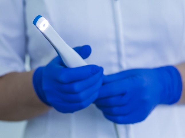 Two gloved hands holding a thin white intraoral camera device