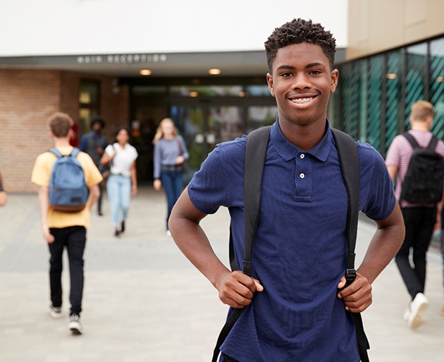 a teen standing outside of a high school and smiling