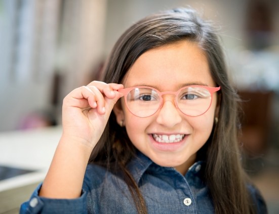 Young girl smiling and touching her glasses
