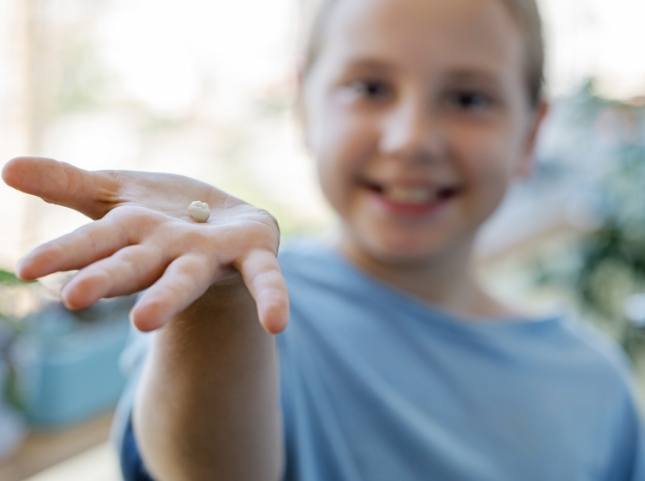 Smiling child holding an extracted tooth in their hand