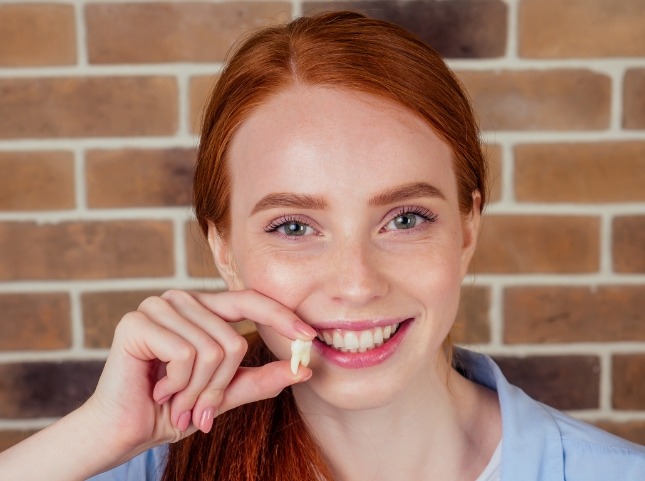 Smiling teenage girl holding an extracted tooth