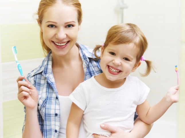Mother and daughter smiling and holding toothbrushes