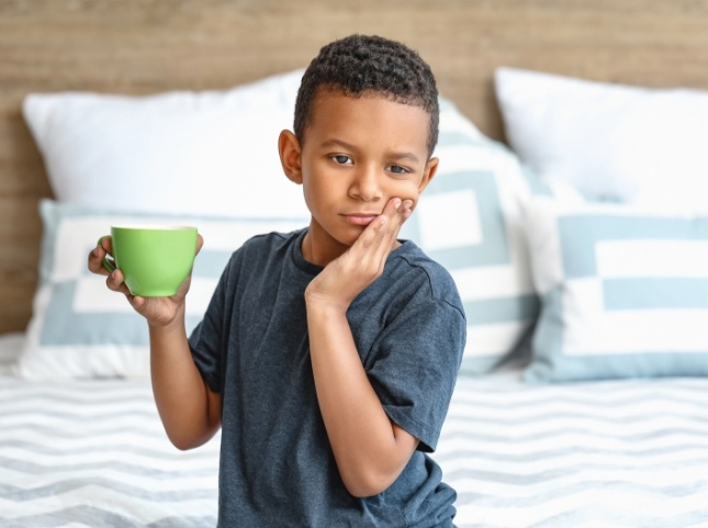 Young boy holding mug and touching his cheek in pain