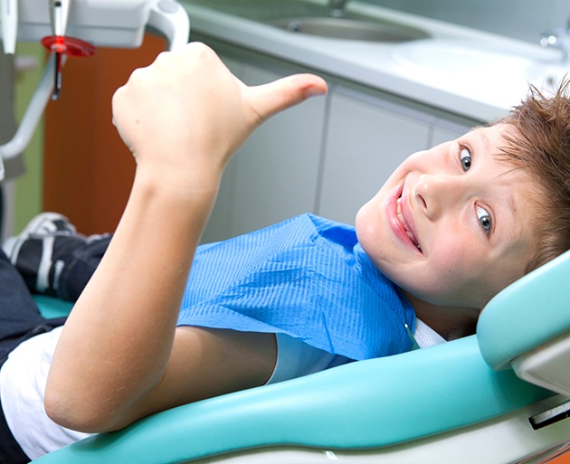 young child smiling and giving thumbs up while in dental chair 