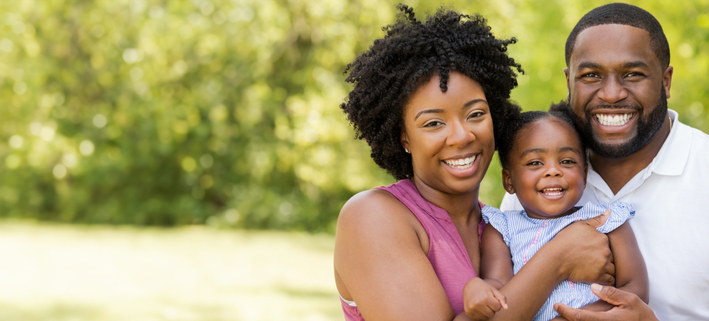 Man and woman smiling outdoors with their baby